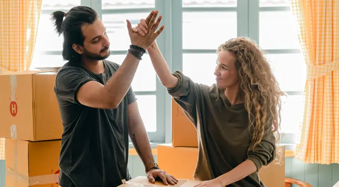 
Young spouses stands next to a stack of boxes giving high fives