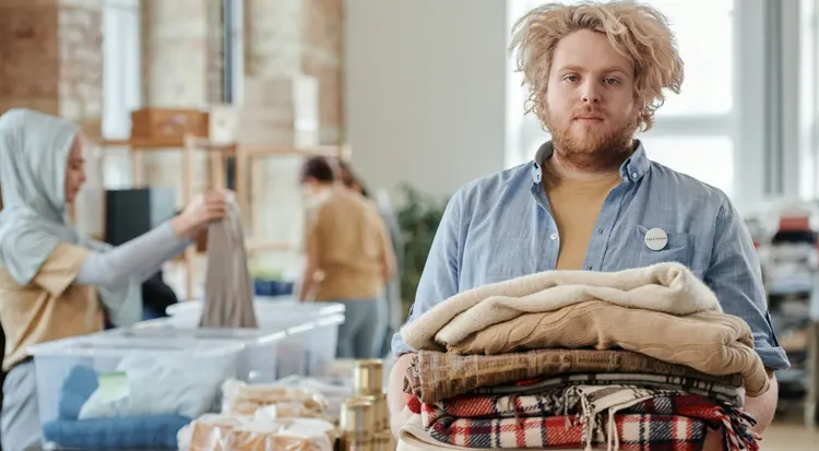 
A bearded man holding a pile of folded scarfs 